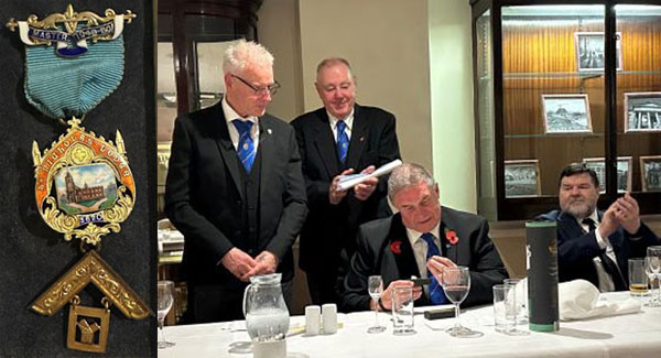 Pictured left: The past master’s jewel. Pictured right: Gary Nicholson (left) presents centenary cufflinks and pin-badge to John, whilst Geoff Bell (centre) and George Anderson (right) look on.