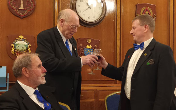 John Bates (standing left) sings the Master’s Song and toasts Richard Dennison with Frank Umbers (seated left). John Bates (standing left) sings the Master’s Song and toasts Richard Dennison with Frank Umbers (seated left).